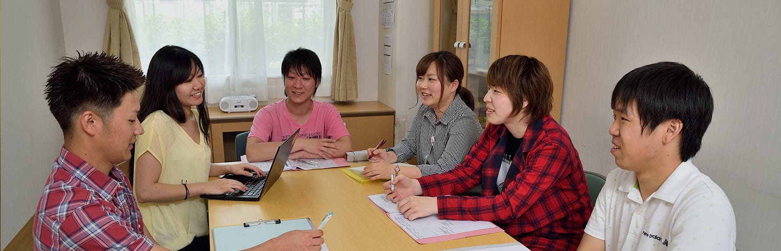 複数の若者が円卓に集まり、レクリエーション活動や会議を行っている室内風景